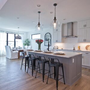 two tone farmhouse kitchen design with white perimeter cabinets and black hardware, with a gray island. Two clear glass pendant lights hang above the gray island