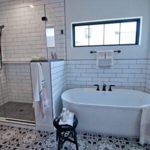 black and white tiled bathroom with large soaking tub on the right, below a window, and separate shower to the left of the tub