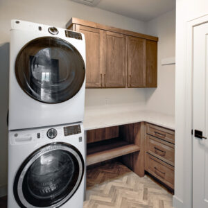 Classic Elegance Functional design laundry room with natural wood cabinets, white quartz countertop, and 3x12 herringbone brick-look porcelain tiles