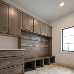 Classic Elegance Design, Laundry room featuring medium wood locker cabinets for storage, white quartz countertops, and 3x12 brick-look porcelain tiles in a herringbone pattern on the floor.