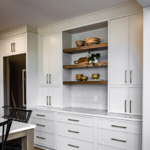Classic Elegance Design, Stylish kitchen coffee bar featuring open natural wood shelving, white fluted tile backsplash, white quartz countertops, and white cabinets with two counter-to-ceiling flanking cabinets for added storage.