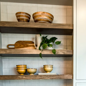 Classic Elegance Coffee bar design featuring open natural wood shelves, a white fluted tile backsplash in the Piano style from Emser’s Pagoni Collection with a linear design, and a sleek white quartz countertop